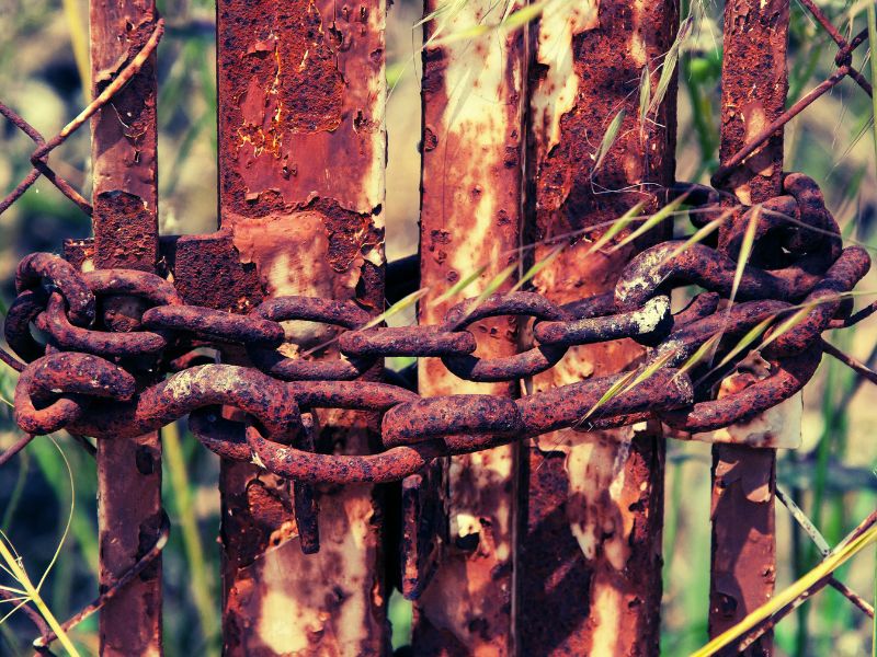 Rusty metal chains around a rusted metal gate. Photo by PIXAMD AMX on Unsplash