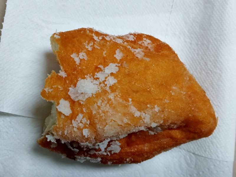 A half-eaten fried dough on a white tissue paper.